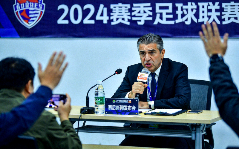 足球比赛赛后新闻发布会场景，主教练正在发言